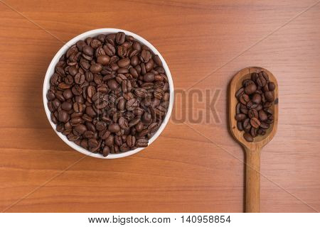 Coffee beans into a bowl and spoon over a wooden table. Coffea arabica