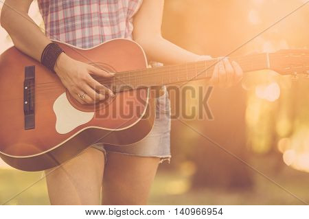Close up of female hands playing acoustic guitar in nature. Retro, music, lifestyle concepts.