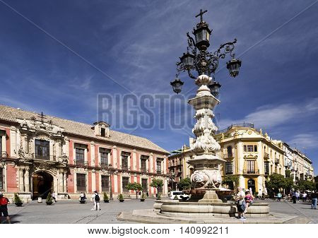 SEVILLE, SPAIN - September 13, 2015: Tourists passing by the marvellous water fountain and lamp at the Plaza Virgen de los Reyes on September 13, 2015 in Seville, Spain