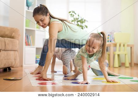 Young Mom Playing Twister Game With Her Children Daughters. Happy Family Have A Fun Time In Holiday