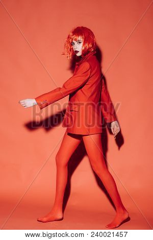 Fashion Concept. Lady With Dark Lips Looking At Camera And Walks. Woman With Makeup And Red Wig Posi