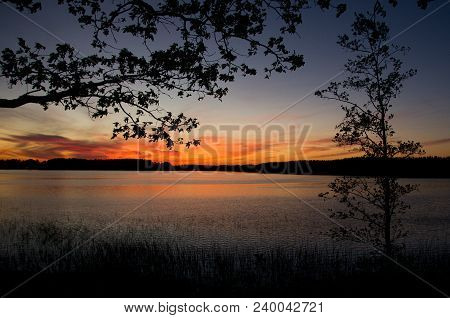 Beautiful Sunset Over Calm Lake. Colorful And Vibrant Landscape Of Lake Shore With Reeds And Trees
