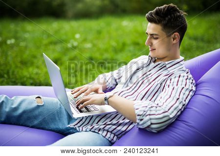 Handsome Man Relax On Inflatable Sofa Lamzac On The Grass With Laptop