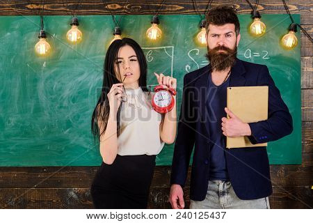 Man With Beard Hold Book And Sexy Girl Teacher Holds Alarm Clock, Chalkboard On Background. Lady Tea