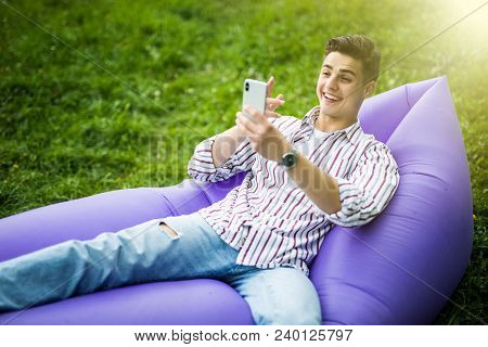 Handsome Young Man Lying On Inflatable Sofa Lamzac Make Video Call On Phone While Resting On Grass I