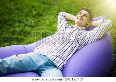Just Relax. Handsome Young Man Lying On Inflatable Sofa Lamzac While Resting On Grass In Park On The