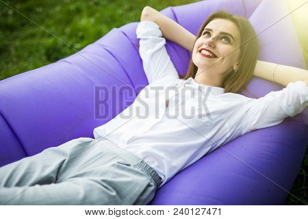 Pretty Young Woman Lying On Inflatable Sofa Lamzac While Resting On Grass In Park On The Sun