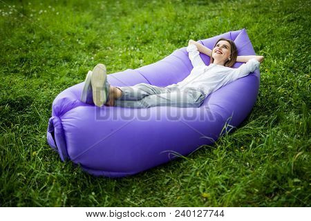 Take A Break. Pretty Young Woman Lying On Inflatable Sofa Lamzac While Resting On Grass In Park On T