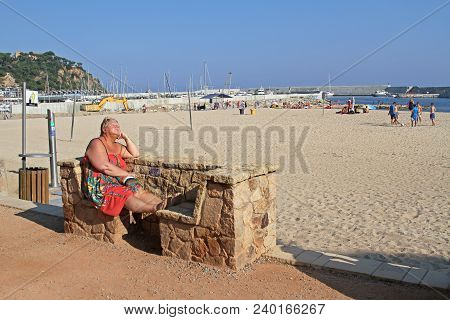 Blanes, Spain - September 11, 2014: Senior Woman Sitting On Stone Bench And Taking Sunbath On Beach 
