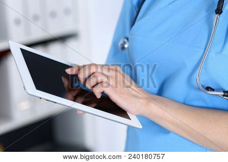 Woman Doctor Using Tablet Computer While Standing Straight In Hospital Office, Closeup. Healthcare, 