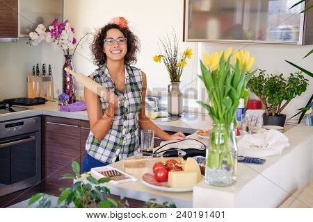 Portrait Of Brunette Attractive Female With Curly Hair In A Home Kitchen With A Lot Of Flowers.