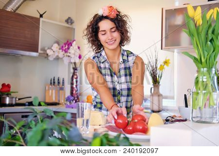 Portrait Of Brunette Attractive Female With Curly Hair In A Home Kitchen With A Lot Of Flowers.