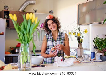 Portrait Of Brunette Attractive Female With Curly Hair In A Home Kitchen With A Lot Of Flowers.