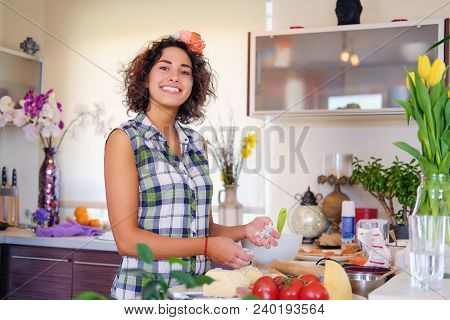 Portrait Of Brunette Attractive Female With Curly Hair In A Home Kitchen With A Lot Of Flowers.