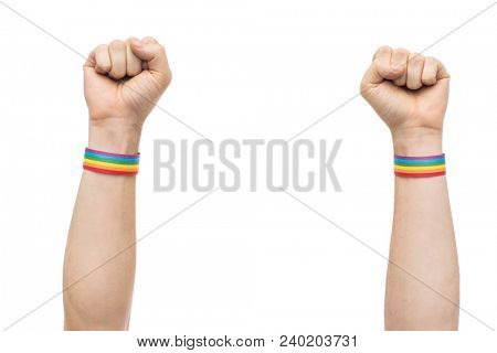 lgbt, same-sex relationships and homosexual concept - close up of male hands wearing gay pride awareness wristbands showing fist