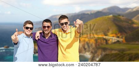 travel, tourism and male friendship concept - group of friends hugging over bixby creek bridge on big sur coast of california background