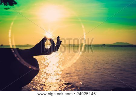 Silhouette, Hand Of Woman Meditating In Yoga Pose Or Lotus Position By The Sea At Sunset. Rear View.