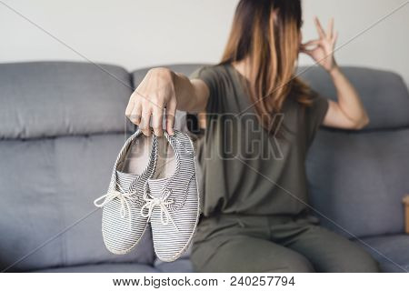 Young Asian Woman Holding A Pair Of Smelly And Stinky Shoes At Home