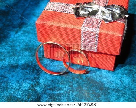 Wedding Rings And Gift Box On Blue Background. Romantic Engagement Concept