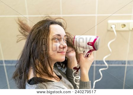Young Woman With Brown Hair Drying Hair With Electric Blowdryer At Home.