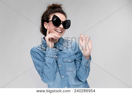 Young Girl In Black Cat Glasses On A Gray Background. Portrait Of A Young Beautiful Girl. Charming G