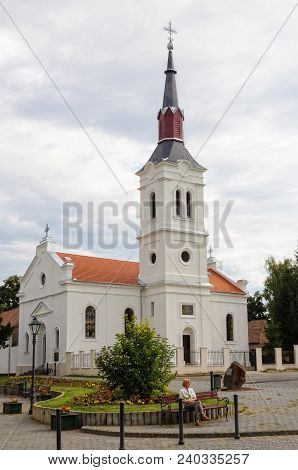 A Tourist Is Enjoying A Quiet Moment On The Bench In Front Of The Evangelical Church - Szecseny, Hun