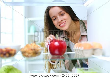 Portrait of female standing near open fridge full of healthy food, vegetables and fruits. Portrait of female