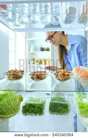 Portrait of female standing near open fridge full of healthy food, vegetables and fruits. Portrait of female