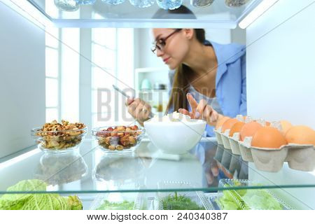 Portrait of female standing near open fridge full of healthy food, vegetables and fruits. Portrait of female