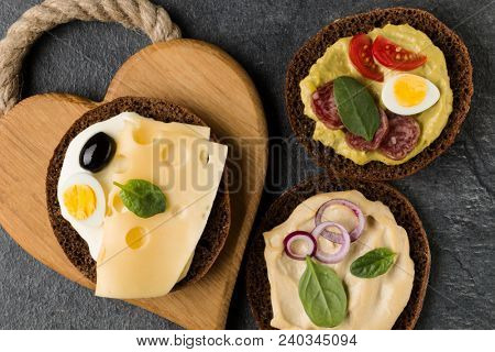 Open  faced  sandwich canape or crostini on a wooden serving board on dark stone background closeup. Top view.