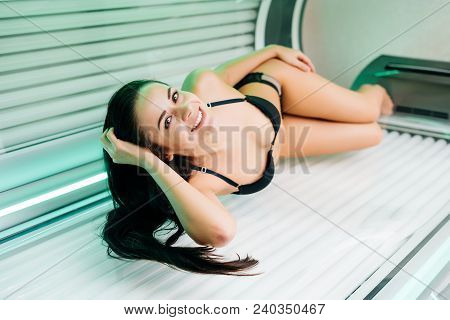 Smiling Slender Girl In A Black Swimsuit Lies In A Horizontal Sunroom And Sunbathing, Wants A Beauti