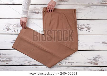Female Hands And Classic Beige Trousers. New Women Trousers On White Wooden Background. Boutique Of 