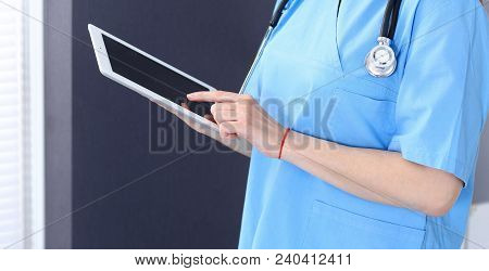 Woman Doctor Using Tablet Computer While Standing Straight In Hospital Office, Closeup. Healthcare, 