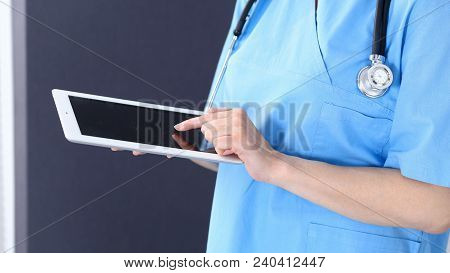 Woman Doctor Using Tablet Computer While Standing Straight In Hospital Office, Closeup. Healthcare, 