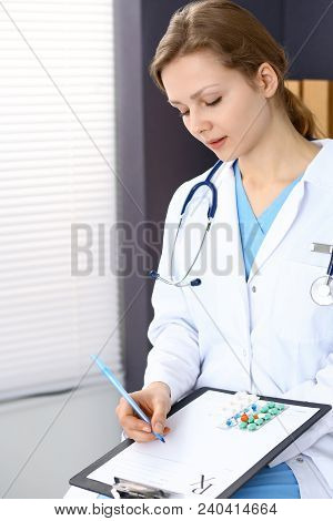 Woman Doctor Write Prescription While Sitting In Hospital Office. A Lot Of Various Colored Pills Liy