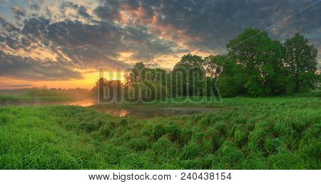 Colorful Summer Morning. Green Field Under Fiolet Clouds. Panoramic Summer Scenic Background.