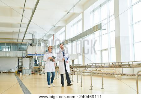 Two Highly Professional Technologists Wearing White Coats Walking Along Production Department Of Mod