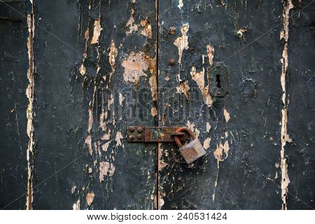 Wooden dark grey door background locked with rusty padlock. Timeworn entrance provides safety and privacy. Close up view with details.