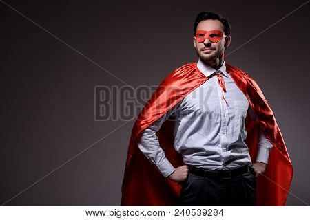 Handsome Super Businessman In Mask And Cape Standing With Hands Akimbo Isolated On Black