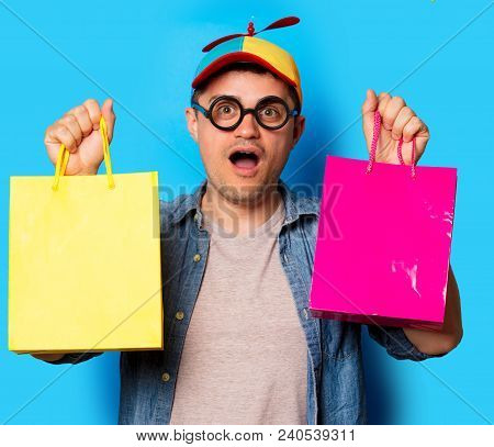 Young Nerd Man With Noob Hat Holding A Shopping Bags On Blue Background