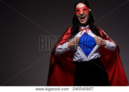 Laughing Attractive Super Businesswoman In Red Cape And Mask Showing Blue Shirt Isolated On Black