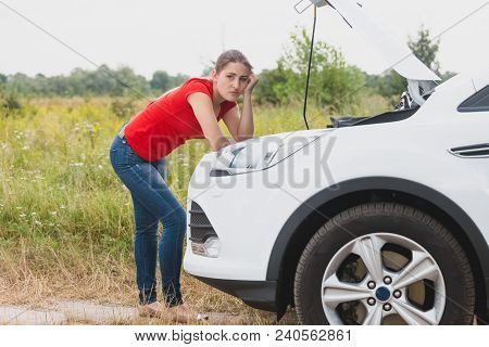 Portrait Of Sad Woman Leaning On Engine Of Broken Car In Field