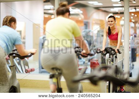 Young fitness instructor in activewear giving advice to her team during training on bikes