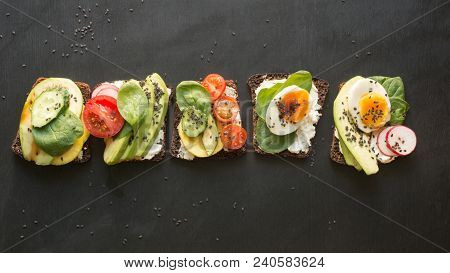 Different Sandwiches With Vegetables, Eggs, Avocado, Tomato, Rye Bread On Black Chalkboard Backgroun