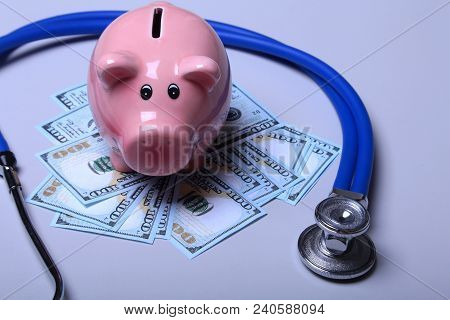 Piggy Bank With Dollar Notes And Stethoscope On A Wooden Desk.