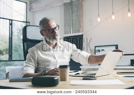Attractive And Confidental Adult Businessman Using Mobile Laptop Computer While Working At The Woode