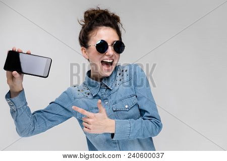 Young Girl In Round Glasses On A Gray Background. Portrait Of A Young Beautiful Girl. Charming Girl 