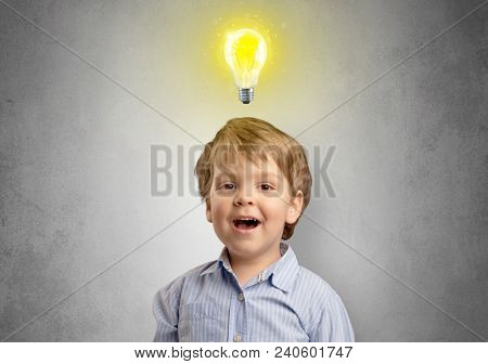 Adorable little kid mull over in front of a grey wall with idea symbol above his head