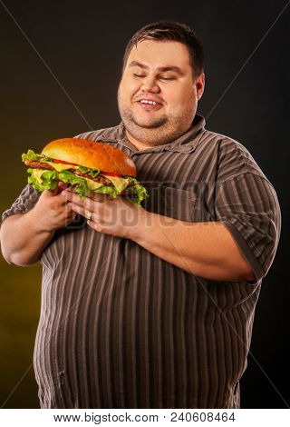 Man eating fast food hamberger. Fat person in large size shirt made great huge hamburger. How to dress well as overweight people concept. Obesity is harmful to health.