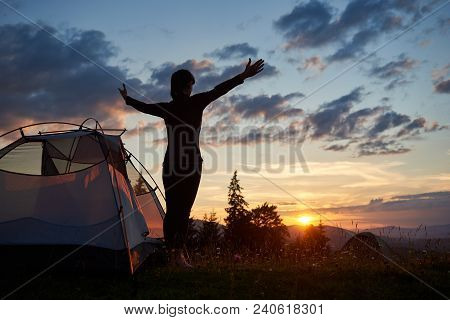 Rear View Silhouette Of Female Standing With Open Arms Near A Camping In The Mountains At Sunrise Un
